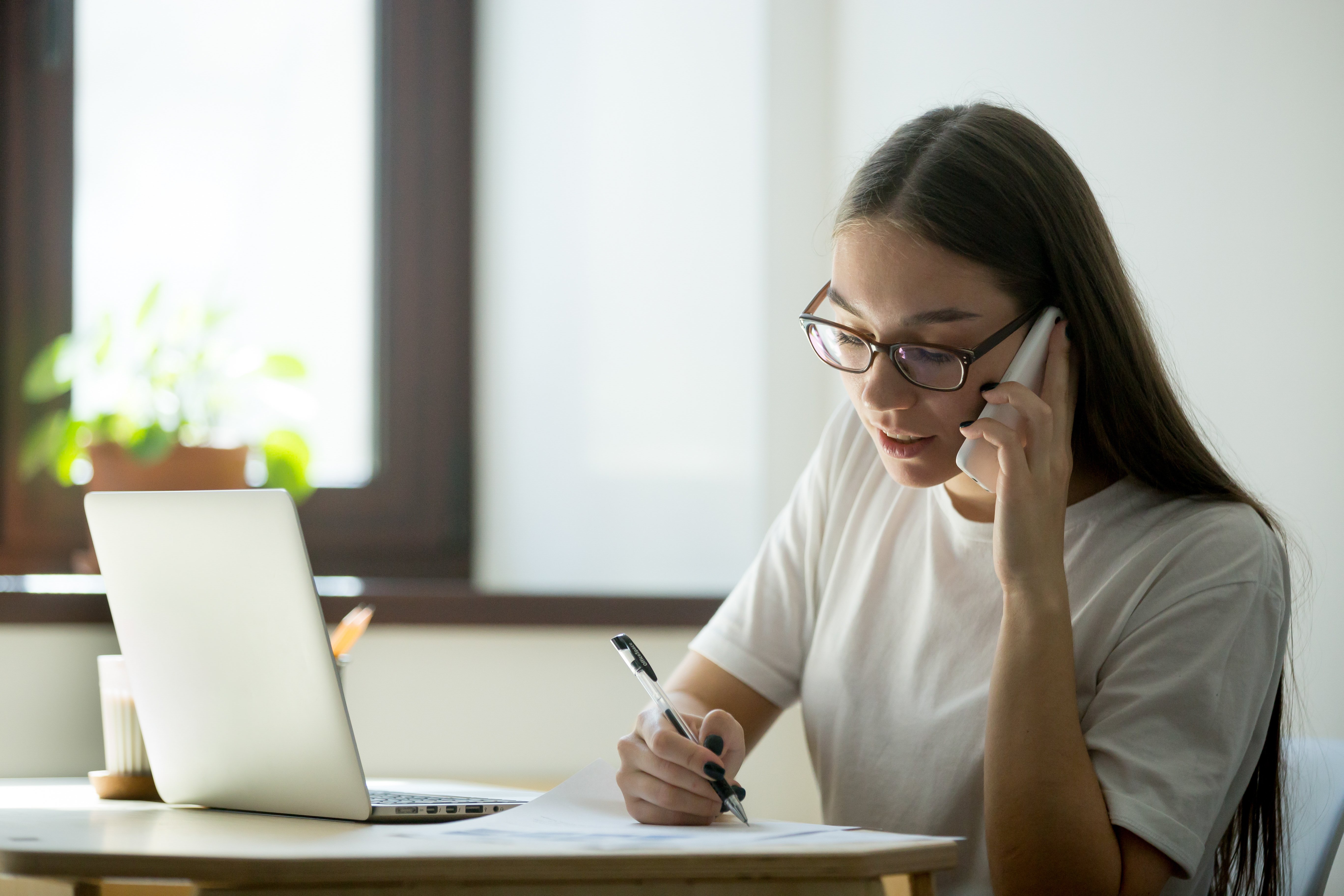 Mujer con lentes hablando por teléfono y trabajando online