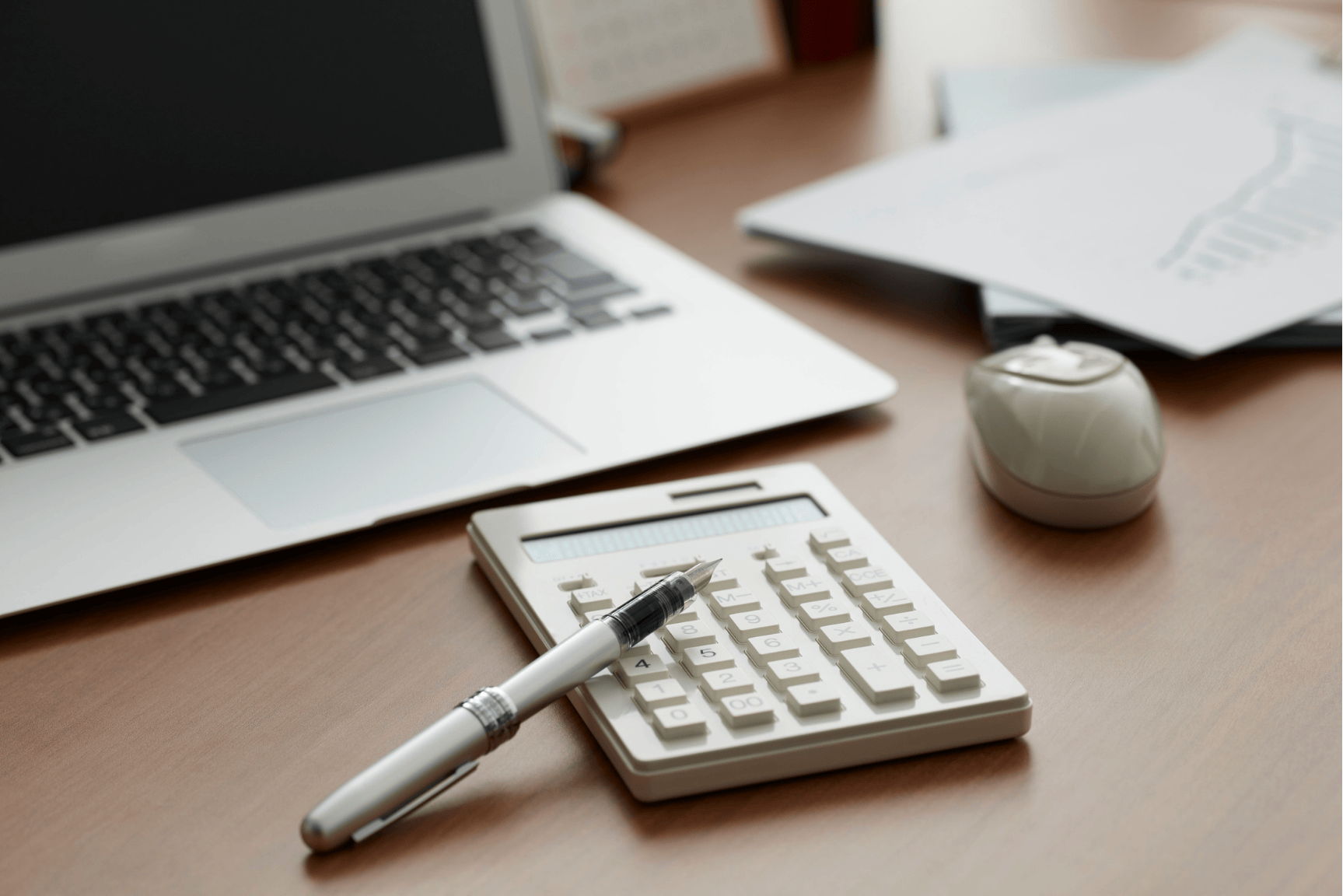 Calculadora, lapicera y computadora sobre un escritorio representando calcular el precio de venta