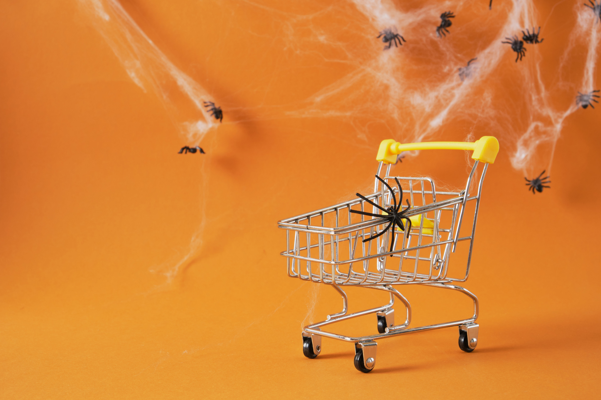 Carrinho de compras com teias e aranhas de brinquedo simbolizando vendas de Halloween no e-commerce