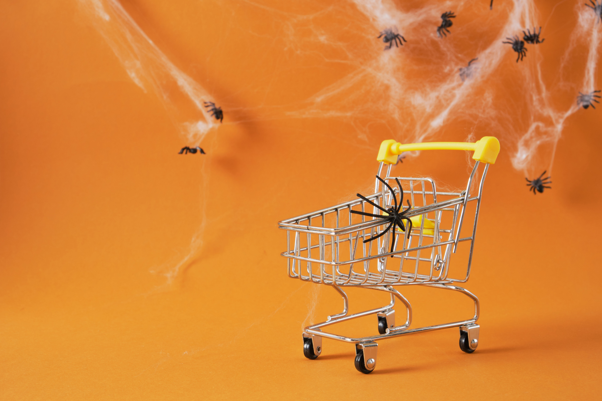 Carrinho de compras com teias e aranhas de brinquedo simbolizando vendas de Halloween no e-commerce