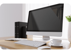 Close de um computador desktop, uma xícara de café e um vaso de flores