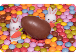 Coelhinhos de felcro sobre confetees de chocolate ao lado de um ovo de Páscoa