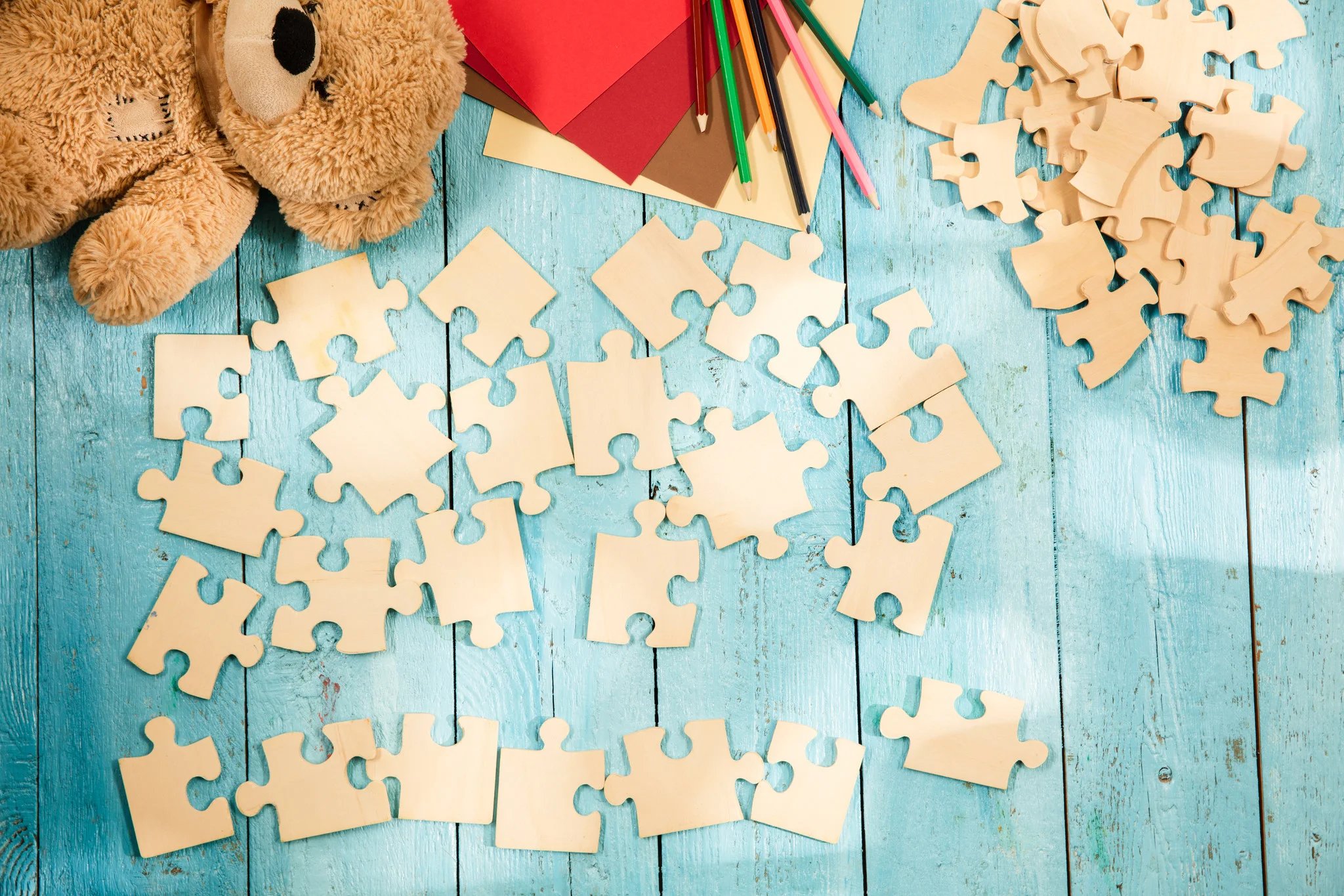 Urso de pelúcia e quebra cabeça de madeira em fundo azul representando oportunidades em brinquedos para vender