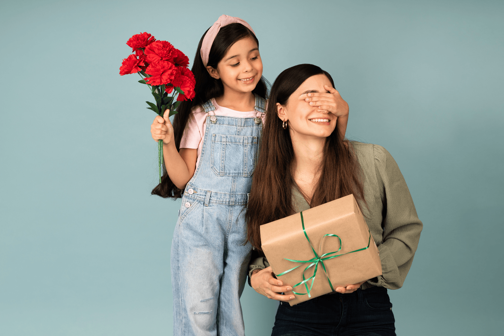 Niña con flores en la mano tapándole los ojos a una mujer que tiene un regalo en las manos representando el Día de la Madre