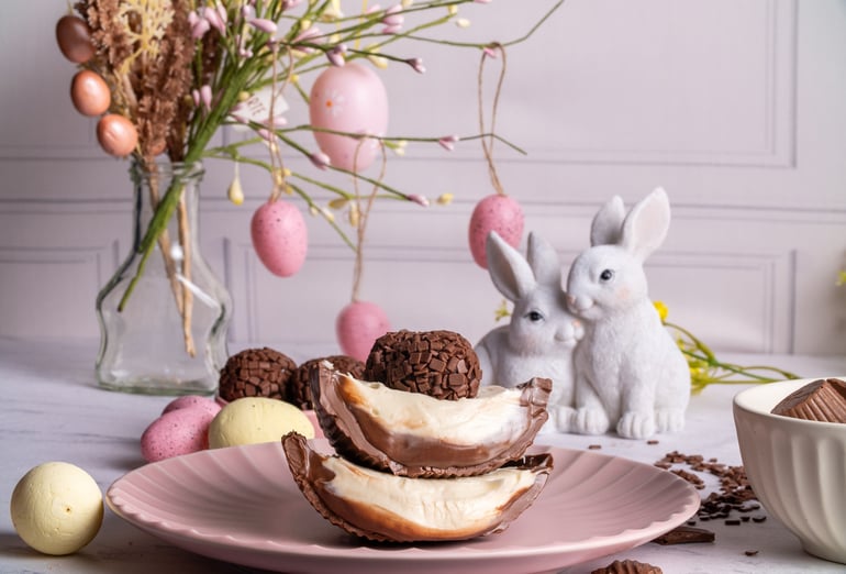 Ovo de Páscoa gourmet brasileiro sobre prato com coelhos de porcelana ao fundo