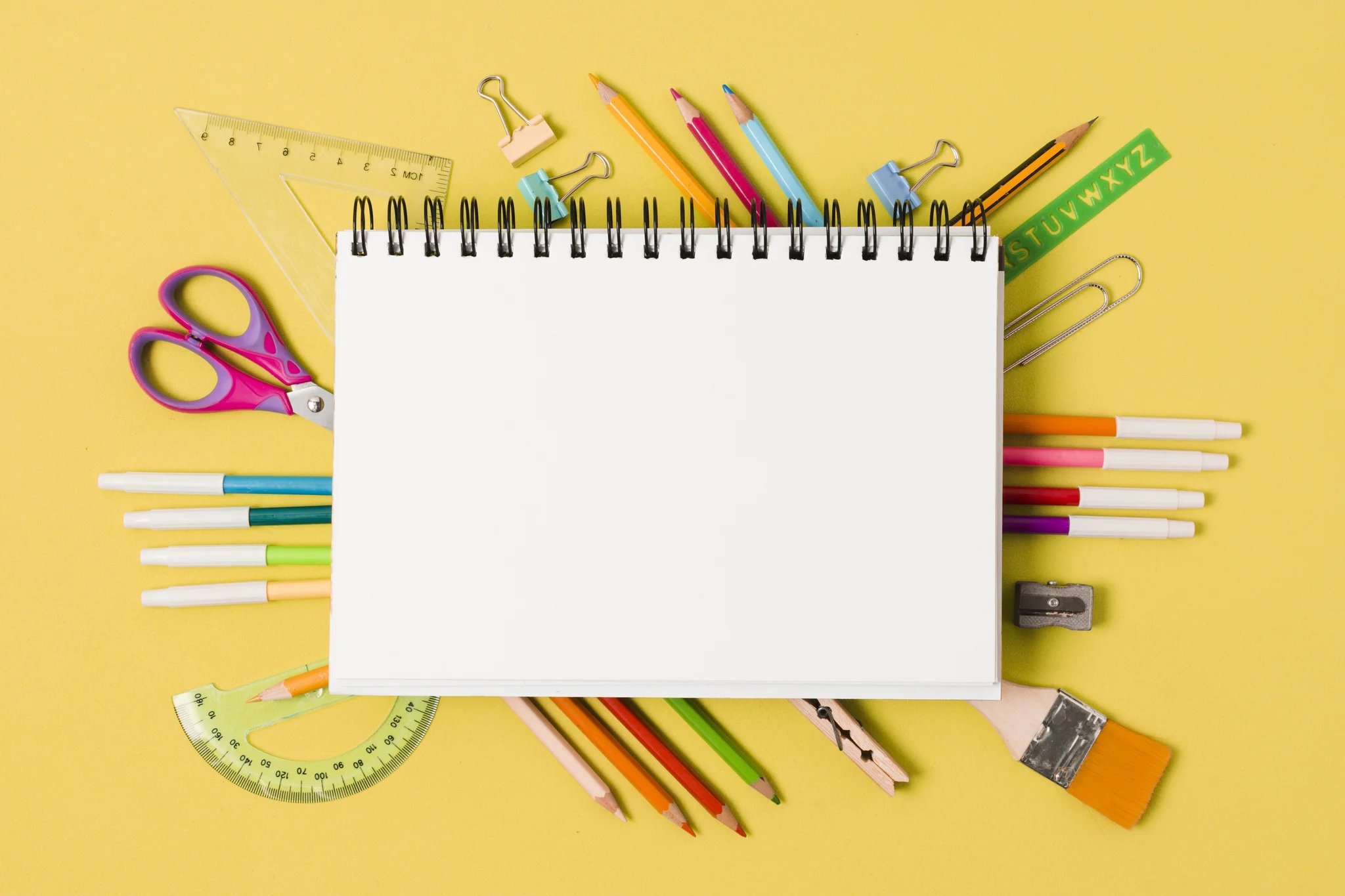 Caderno rodeado por canetinhas, lápis, tesoura e entre outros matérias escolares