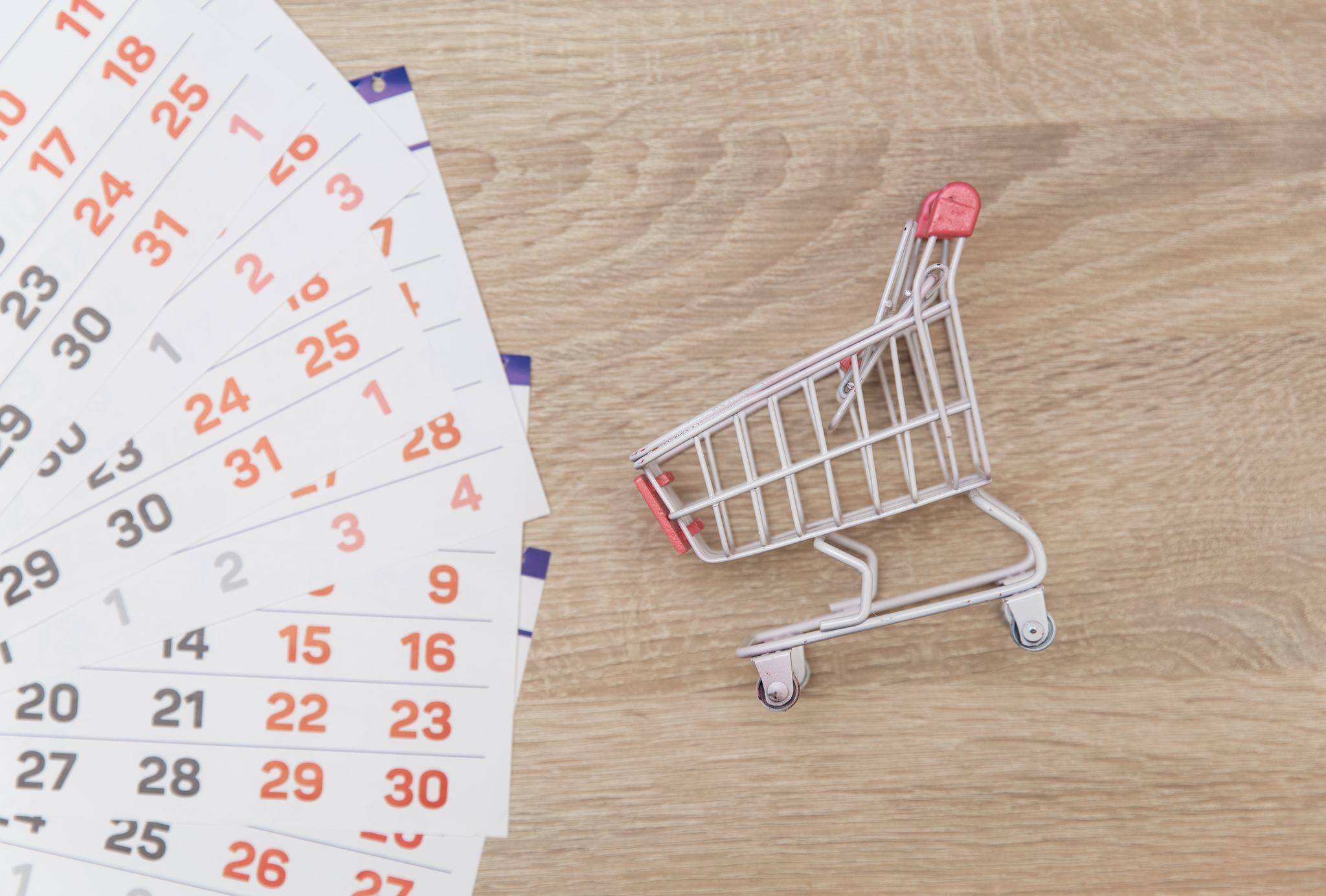 Vista superior de folhas avulsas de calendário com carrinho de compras sobre mesa representando a sazonalidade de vendas online